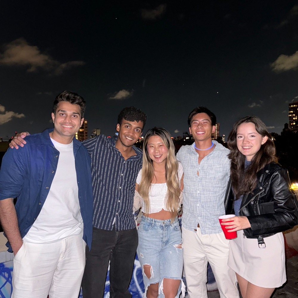 five friends smiling on a rooftop at night