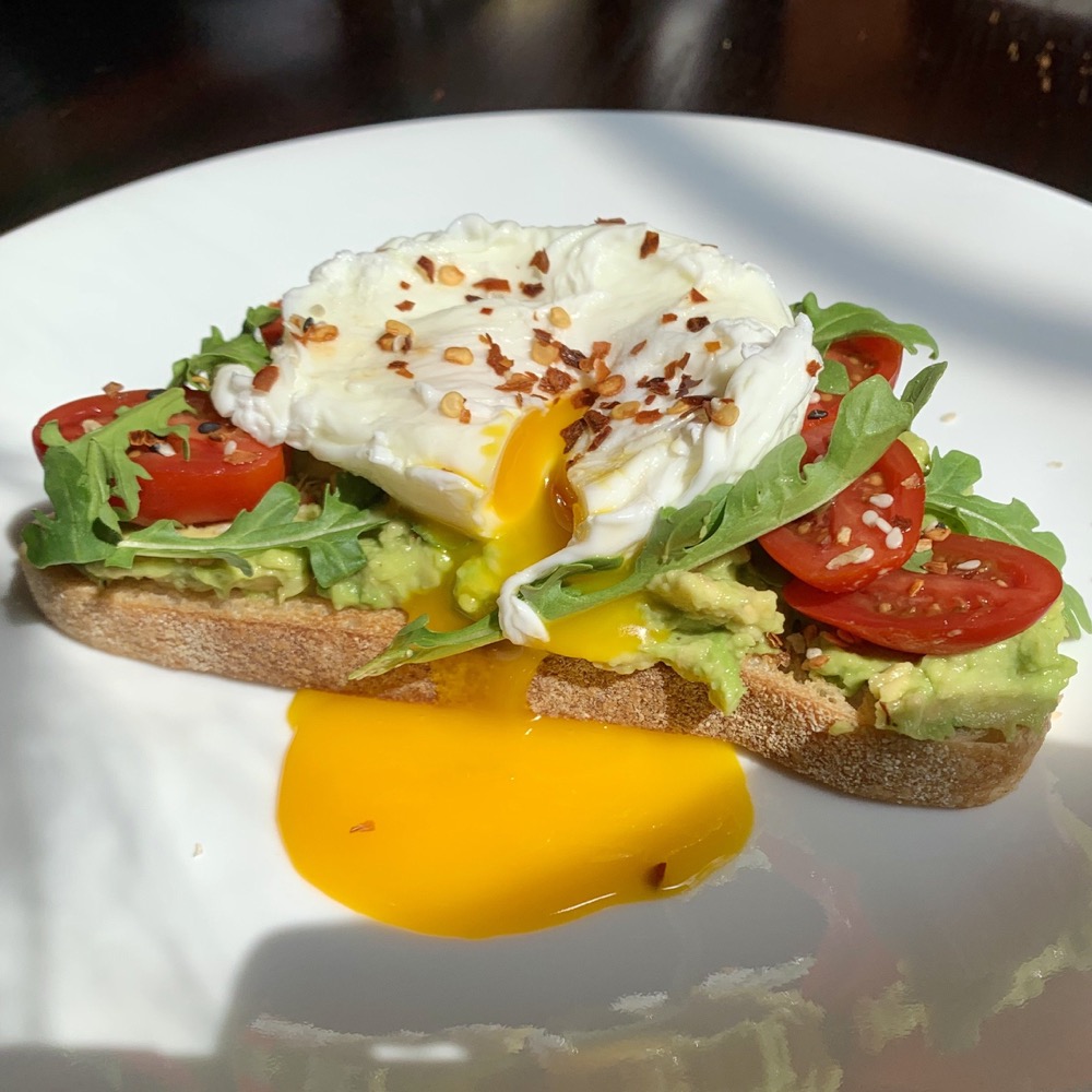 avocado toast with a runny poached egg and tomatoes