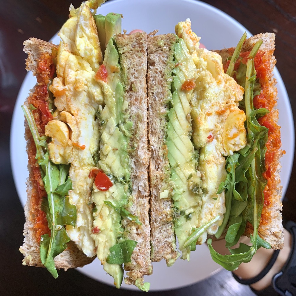 egg, avocado, and arugula sandwich halves on a plate